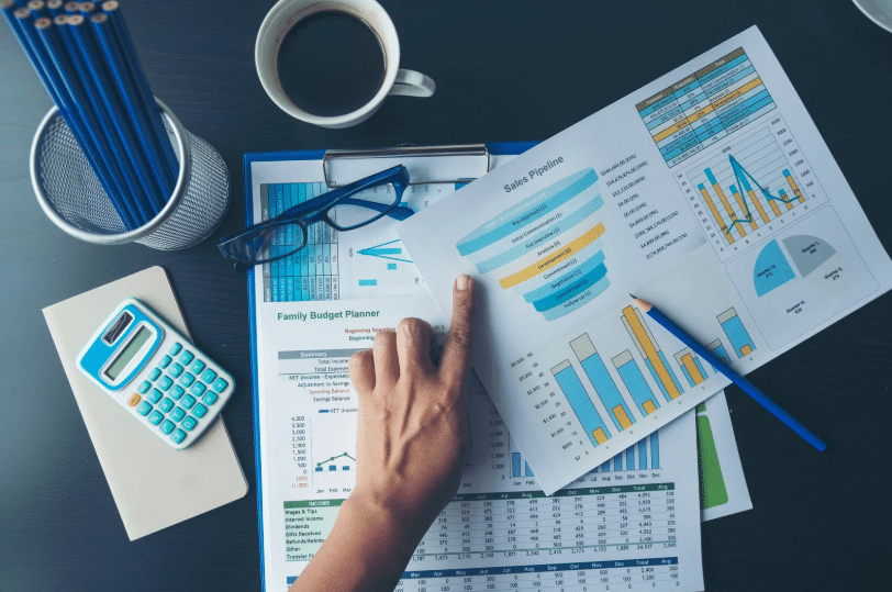 A person pointing at a sales pipeline chart surrounded by financial documents, a calculator, and a coffee cup, highlighting financial planning for quicken vs quickbooks evaluations.